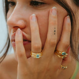 Close-up of a person wearing gold rings with turquoise stones, holding their face.