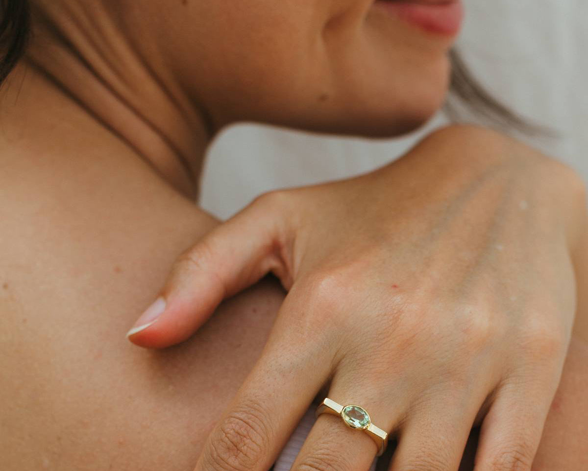 Close-up of a woman's hand with a gold ring on her finger, touching her shoulder.