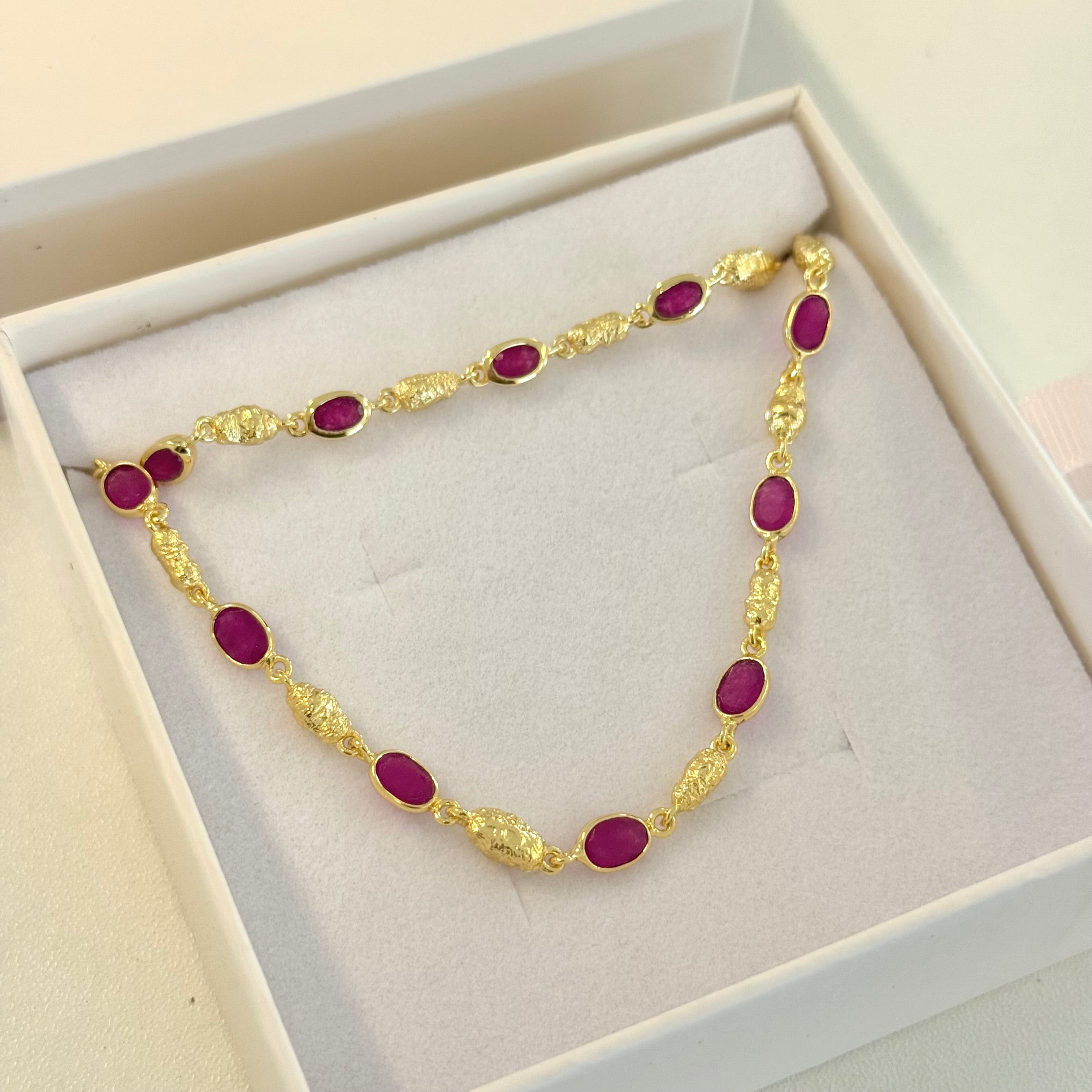 Gold bracelet with red gemstones in a white box