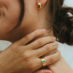 Close-up of a person wearing gold earrings and a ring, with a blurred background.