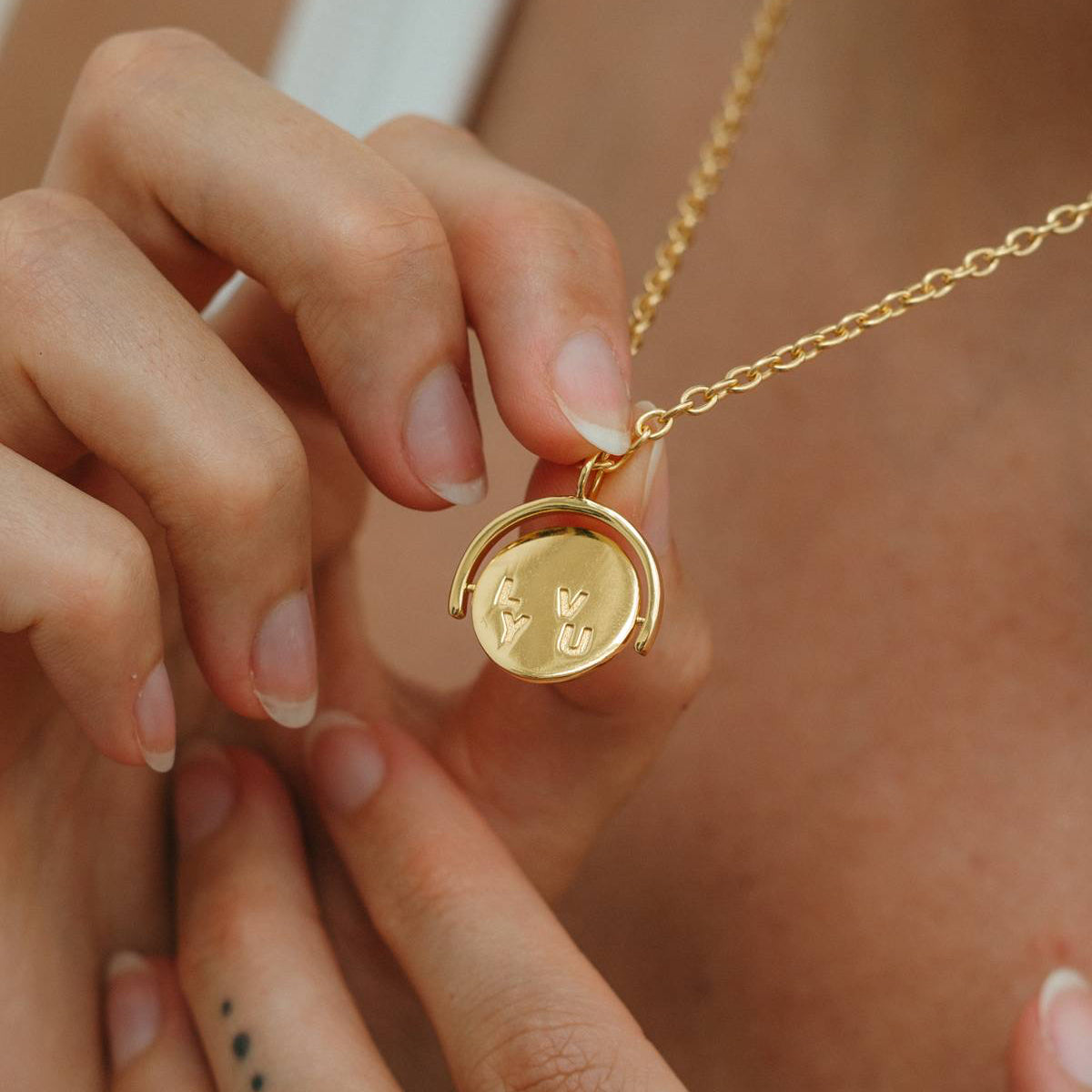 Gold necklace with a pendant held by hands against a neutral background