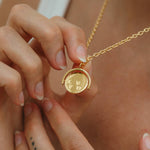 Gold necklace with a pendant held by hands against a neutral background