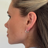 Close-up of a person wearing a silver hoop earring on a plain background