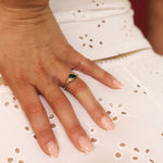 Hand wearing a gold ring with a green gemstone on a white lace fabric background