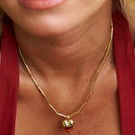 Close-up of a gold necklace with a pendant on a person wearing a red garment.