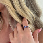 Close-up of a hand with a ring featuring a blue gemstone, touching blonde hair.