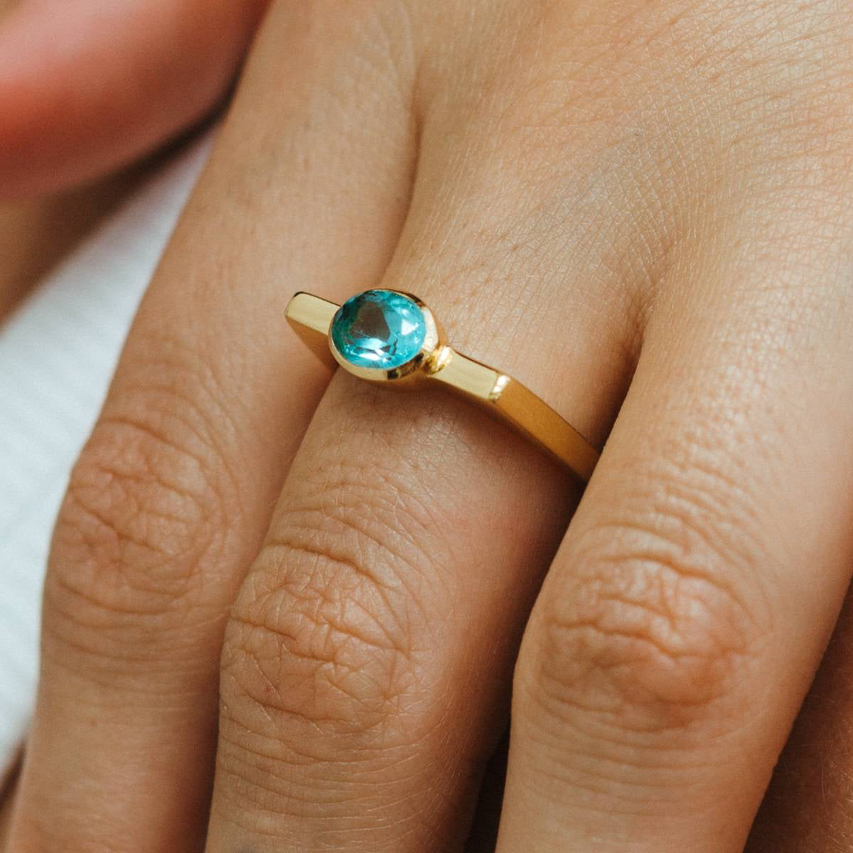 Gold ring with a blue gemstone on a person's finger