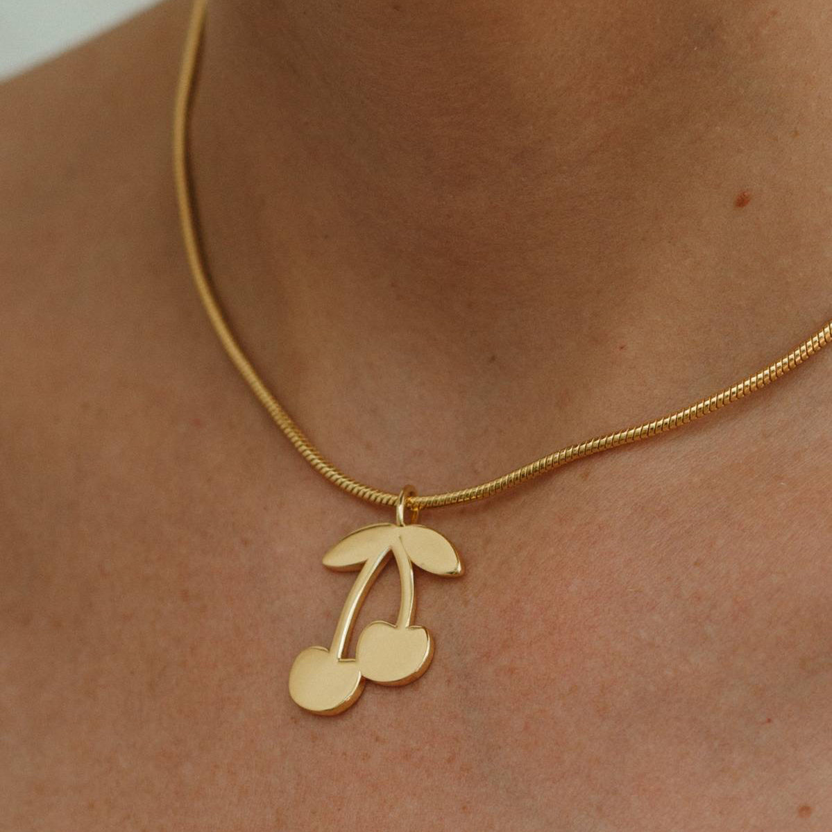 Gold necklace with a cherry pendant on a person's neck