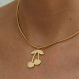 Gold necklace with a cherry pendant on a person's neck