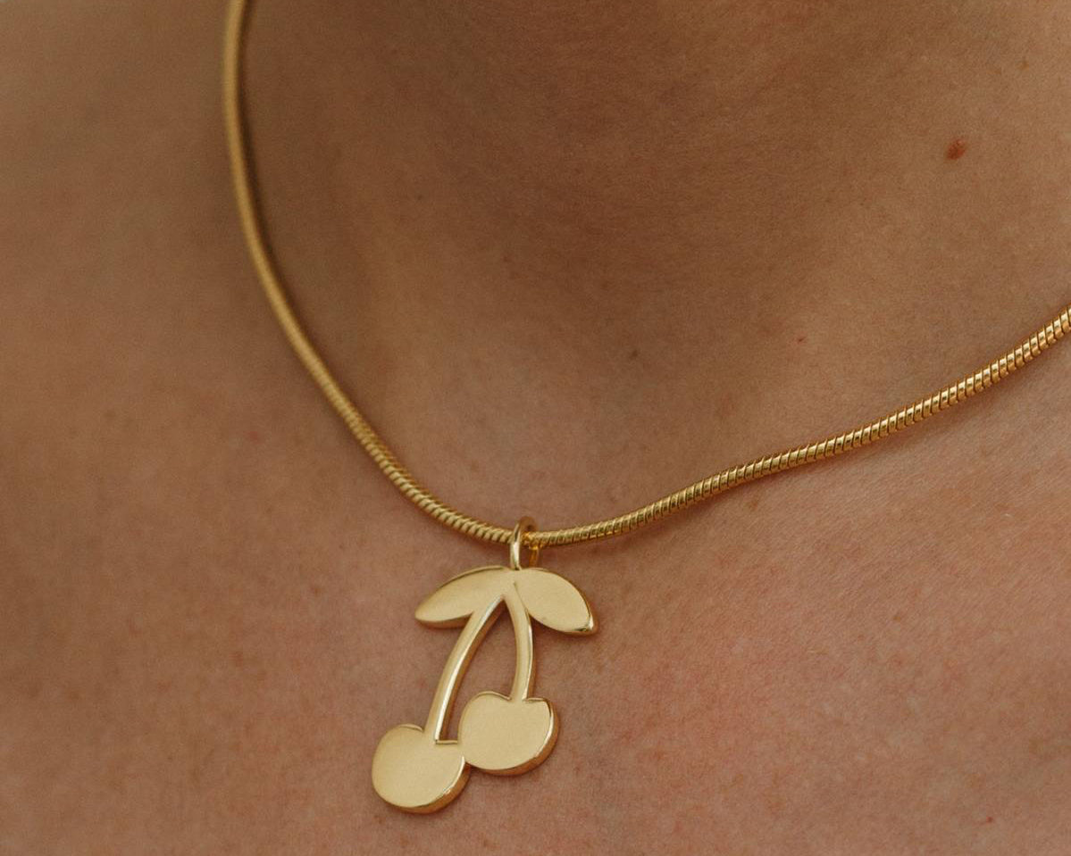 Gold necklace with a cherry pendant on a person's neck