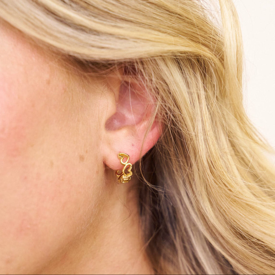 Close-up of a person wearing gold hoop earrings with a blurred background