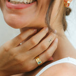 Woman wearing gold earrings and rings, smiling with a neutral background