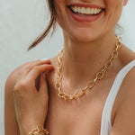 Woman wearing a gold chain necklace and bracelet against a neutral background