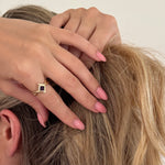 Close-up of a hand with a ring on a person's head, with a neutral background