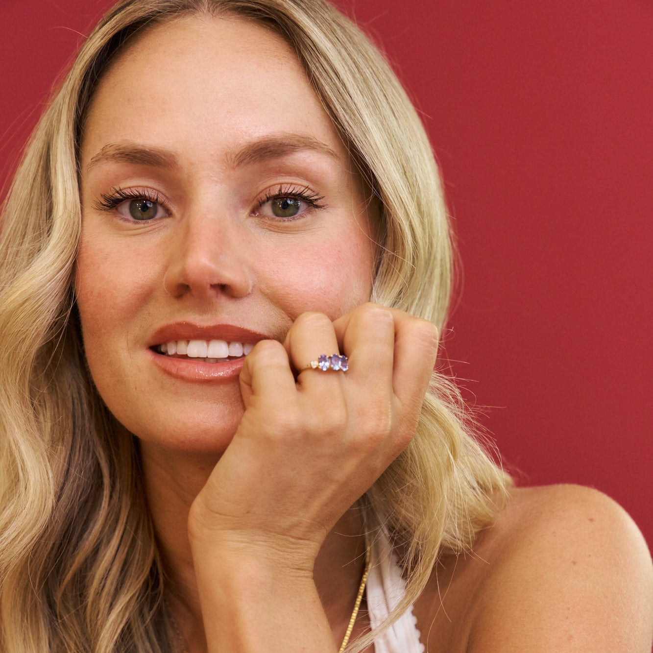 Woman with blonde hair and a ring on her finger against a red background