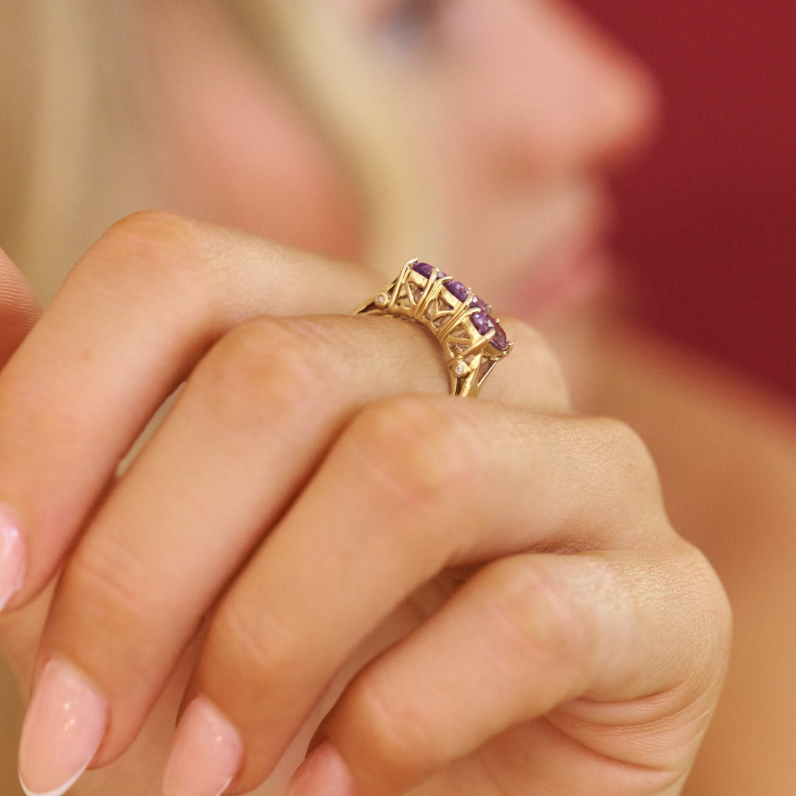 Gold ring with purple gemstones on a person's finger against a blurred background