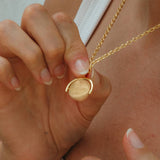 Gold necklace with a round pendant held by a hand against a neutral background