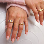 Close-up of hands wearing gold rings with gemstones on a light background