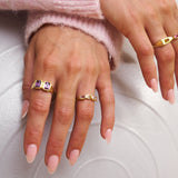 Close-up of hands wearing gold rings with gemstones on a light background