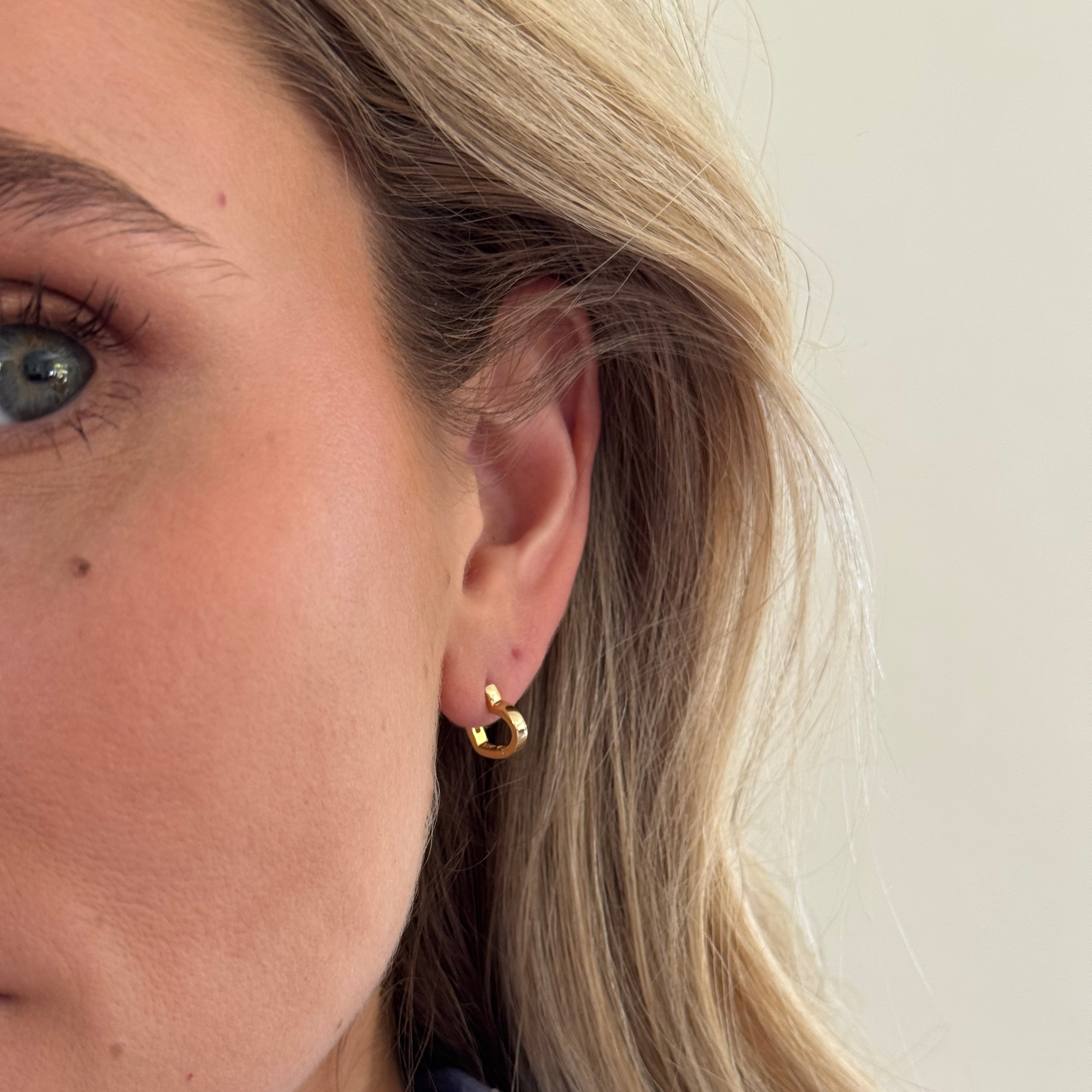 Close-up of a person wearing a gold earring with a plain background
