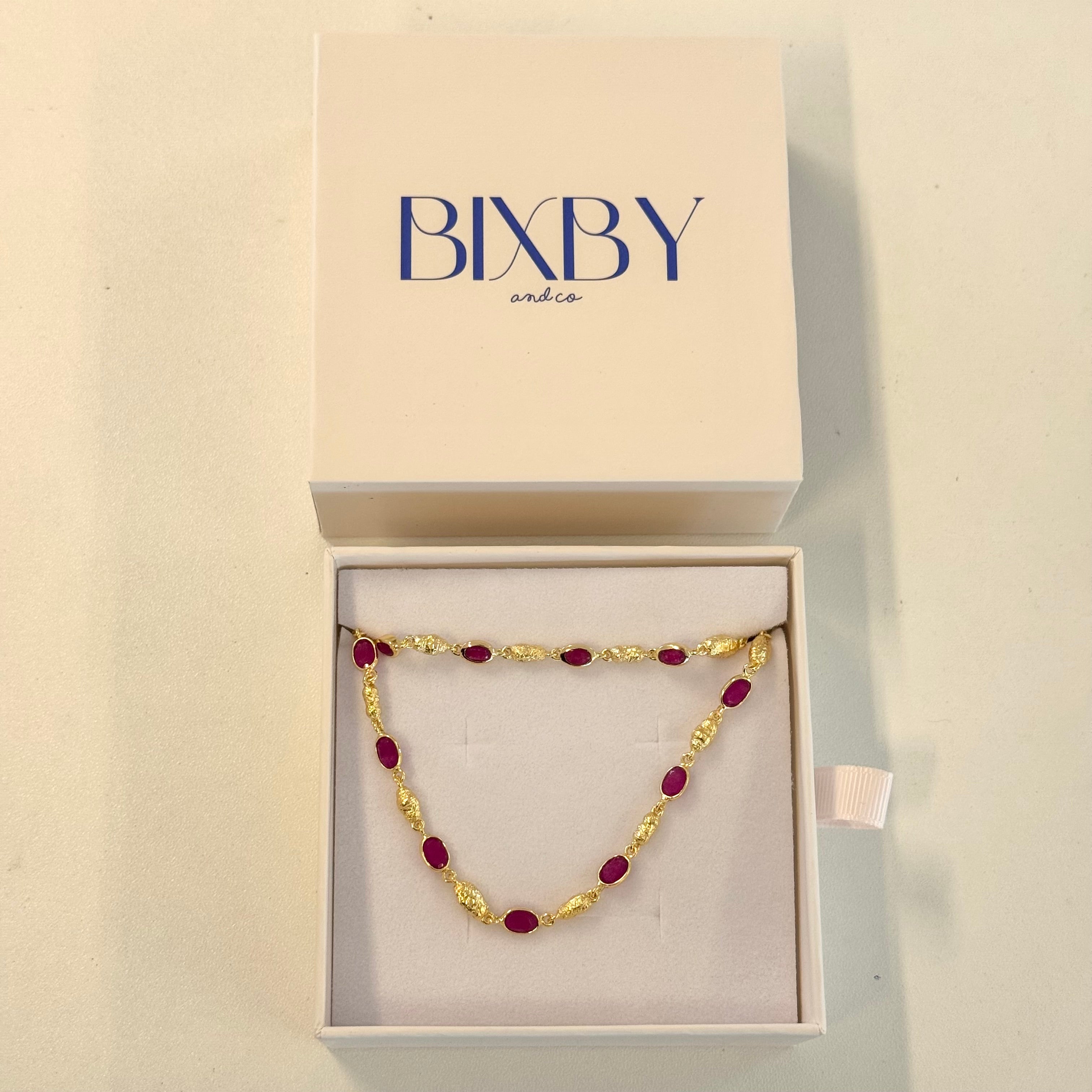 Gold and red beaded necklace in a Bixby box on a beige background