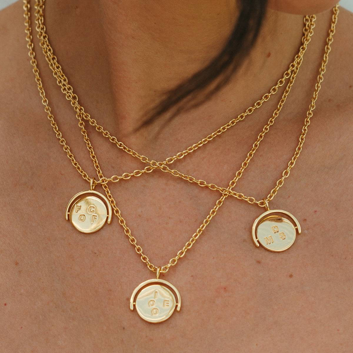 Close-up of a person wearing gold necklaces with circular pendants.