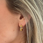 Close-up of a person wearing a gold earring with three stones.