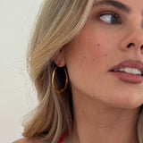 Close-up of a woman wearing a gold hoop earring against a neutral background