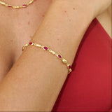 Gold necklace and bracelet with red stones worn by a person against a red background