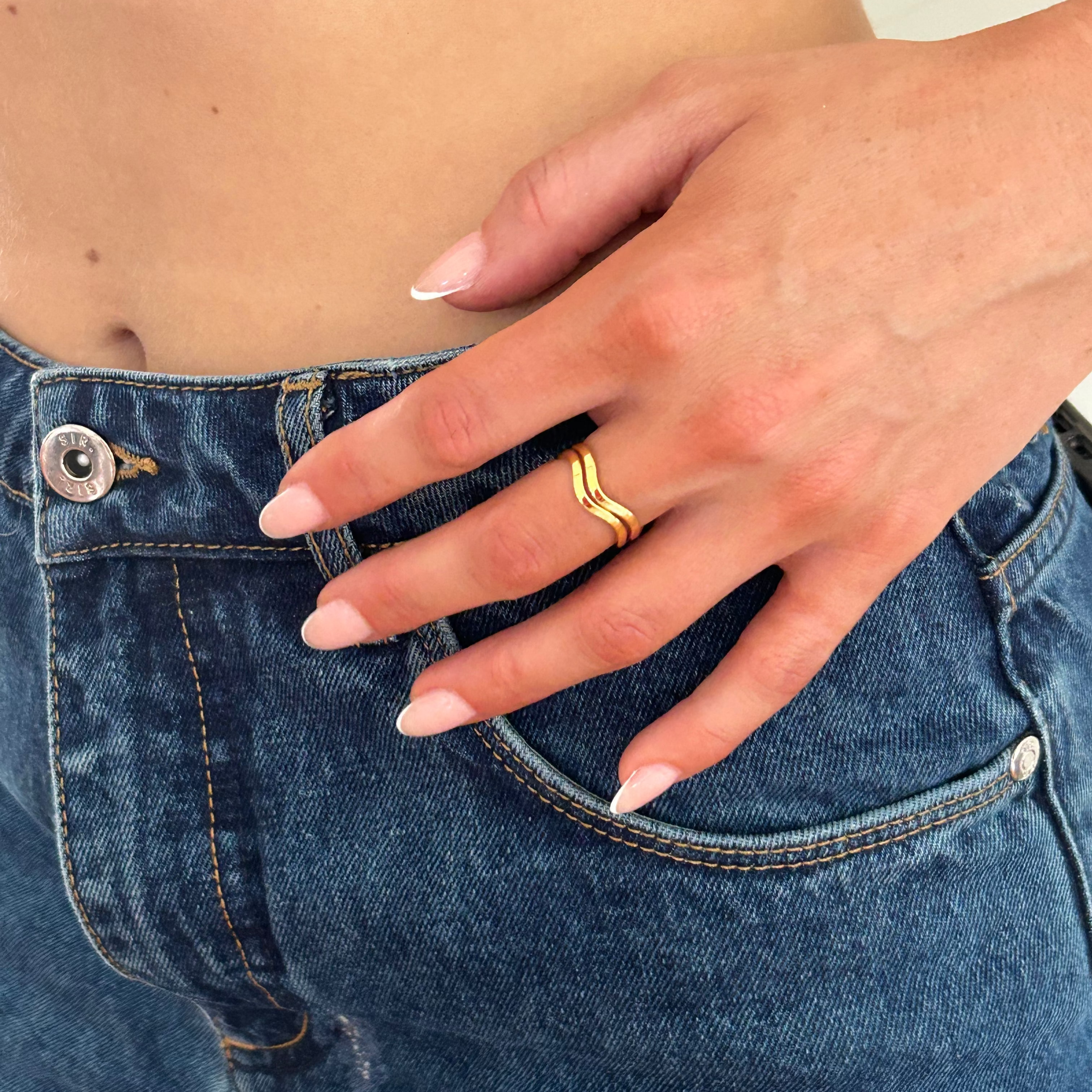 Person wearing blue jeans with a hand on the waist, wearing a gold ring.