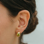 Close-up of an ear wearing a green gemstone earring against a neutral background