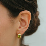 Close-up of an ear wearing a green gemstone earring against a neutral background