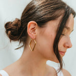 Woman wearing gold geometric hoop earrings against a neutral background
