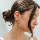 Woman wearing gold geometric hoop earrings against a neutral background