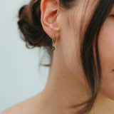 Close-up of a person wearing green earrings with a neutral background