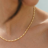 Close-up of a person wearing a gold necklace against a neutral background