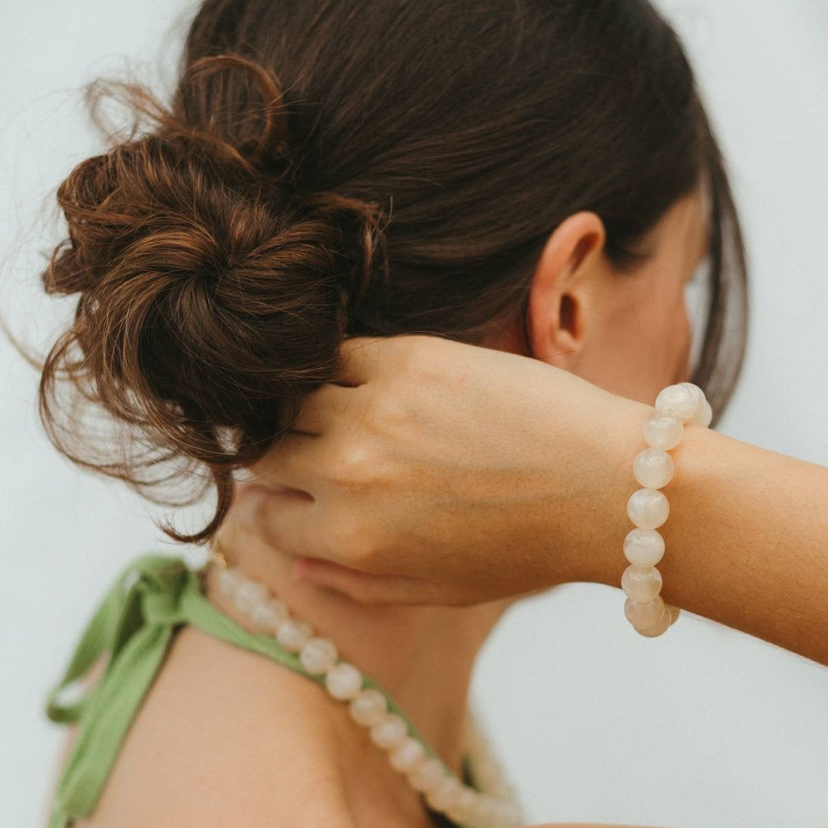 Woman with a bun and white beaded bracelet on a plain background