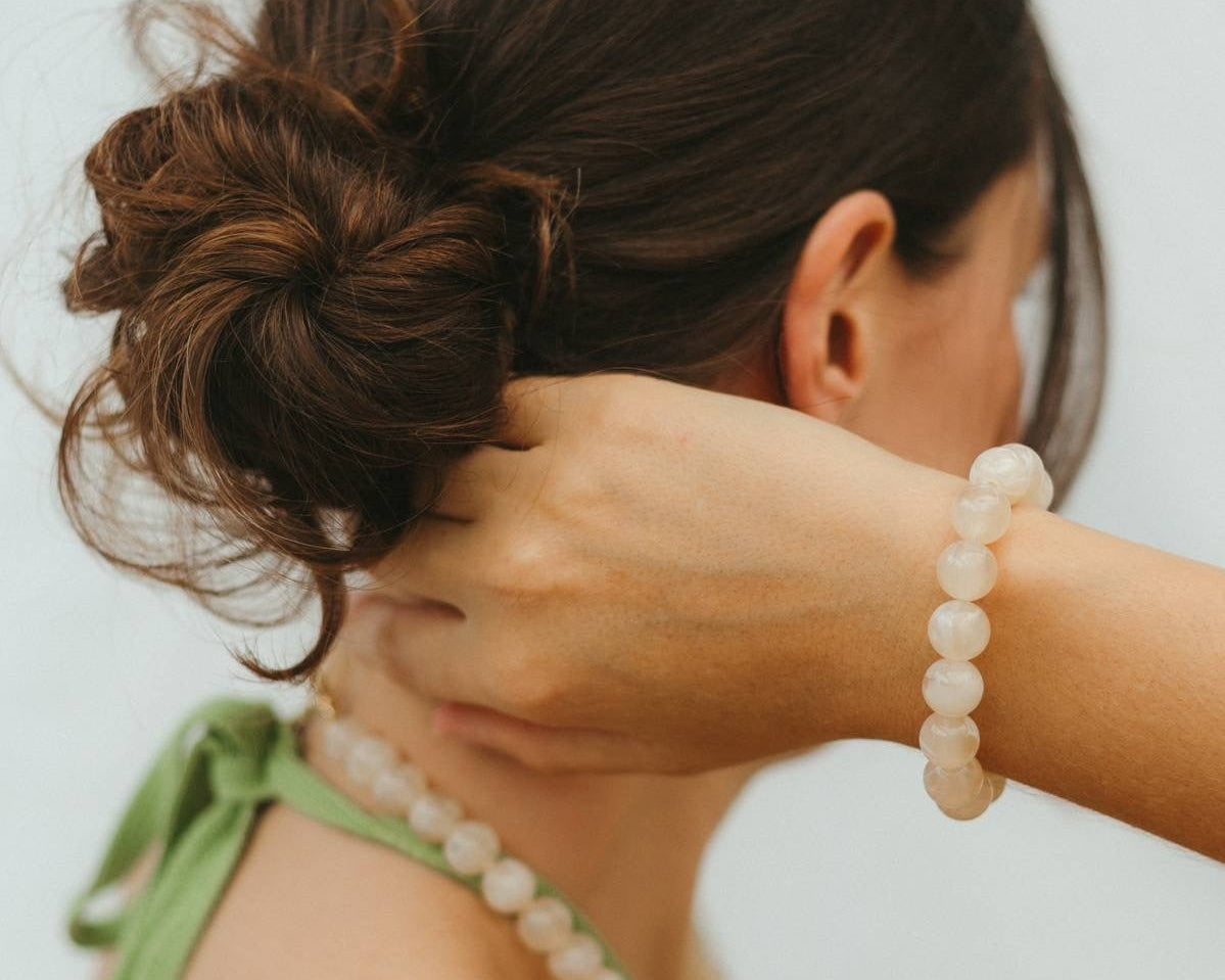Woman with a bun and white beaded bracelet on a plain background