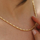 Gold necklace being worn on a person's neck with a close-up view.