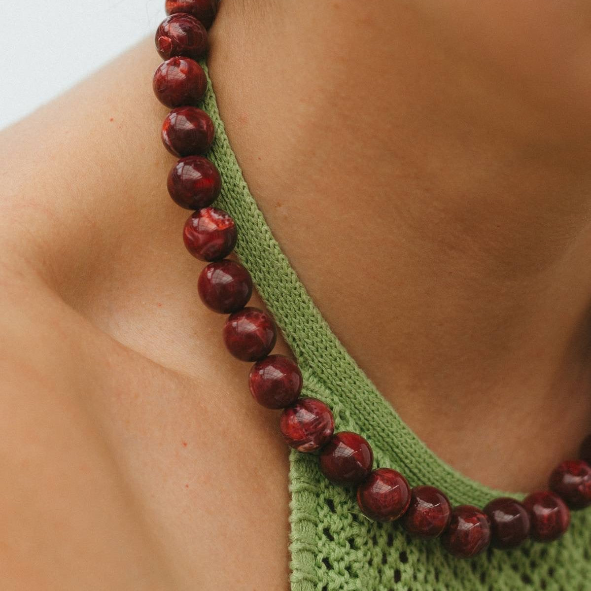 Close-up of a person wearing a green top with a red beaded necklace.