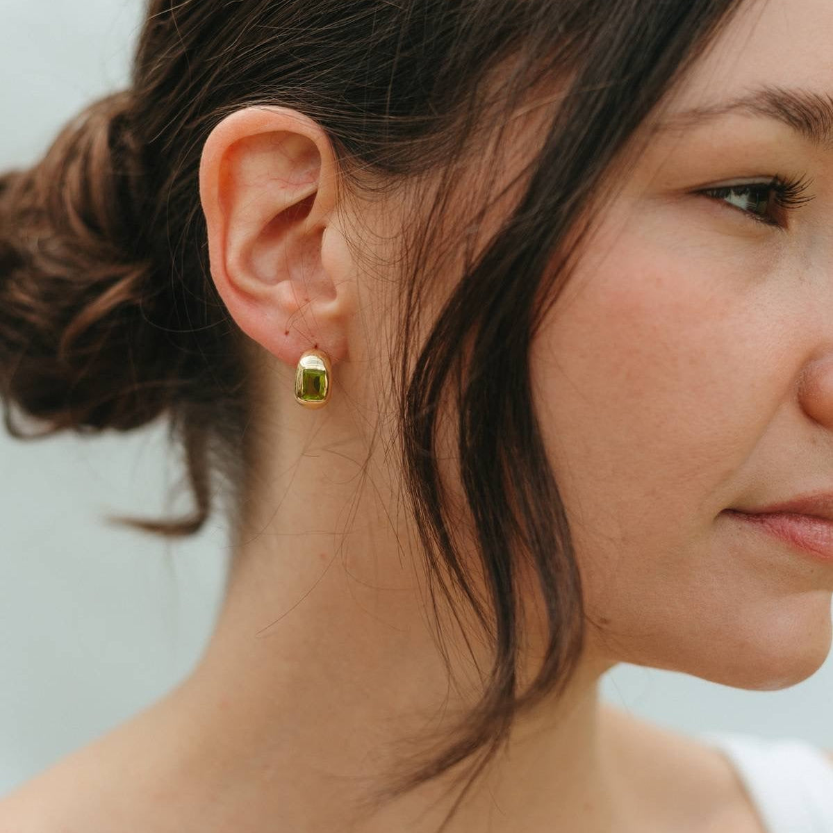 Close-up of a woman wearing a gold earring with a green gemstone against a neutral background