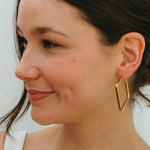 Woman wearing gold geometric hoop earrings against a neutral background
