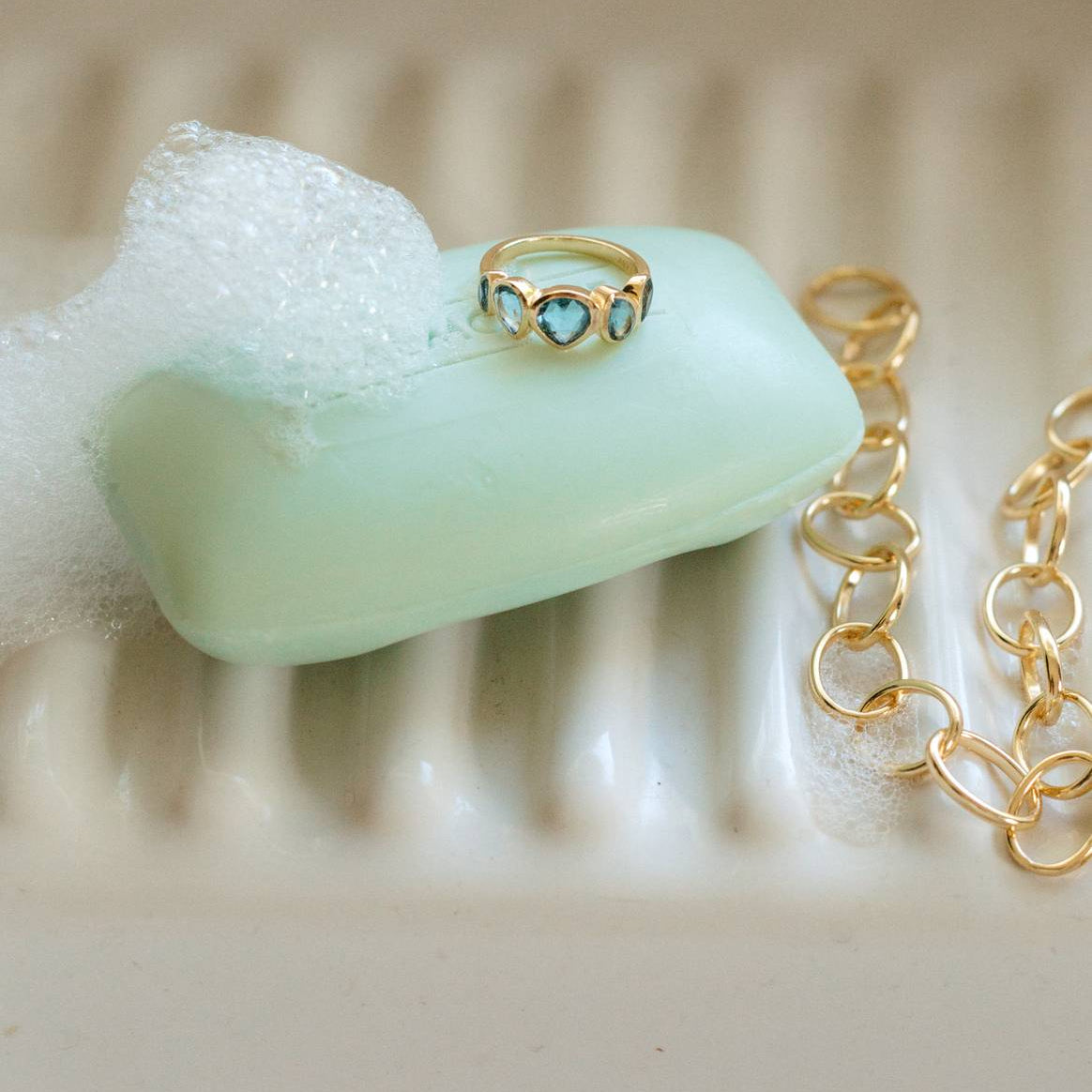 Gold ring with a blue gemstone on a bar of soap next to a gold chain.