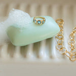 Gold ring with a blue gemstone on a bar of soap next to a gold chain.