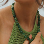 Close-up of a person wearing a green knitted top and a green beaded necklace.