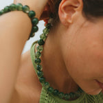 Person wearing a green beaded necklace and bracelet, with a blurred background
