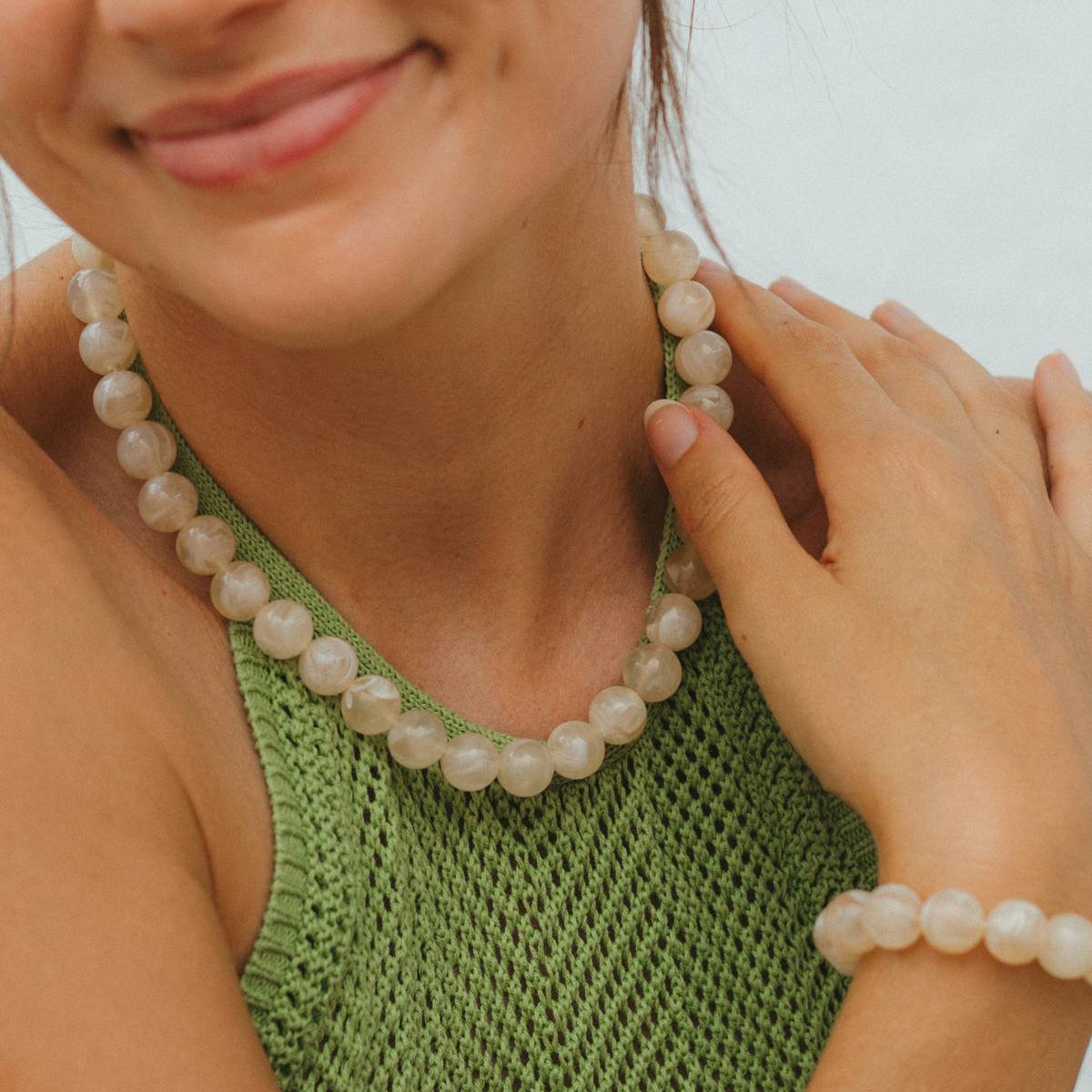 Woman wearing a green knitted top and beaded necklace with a blurred background