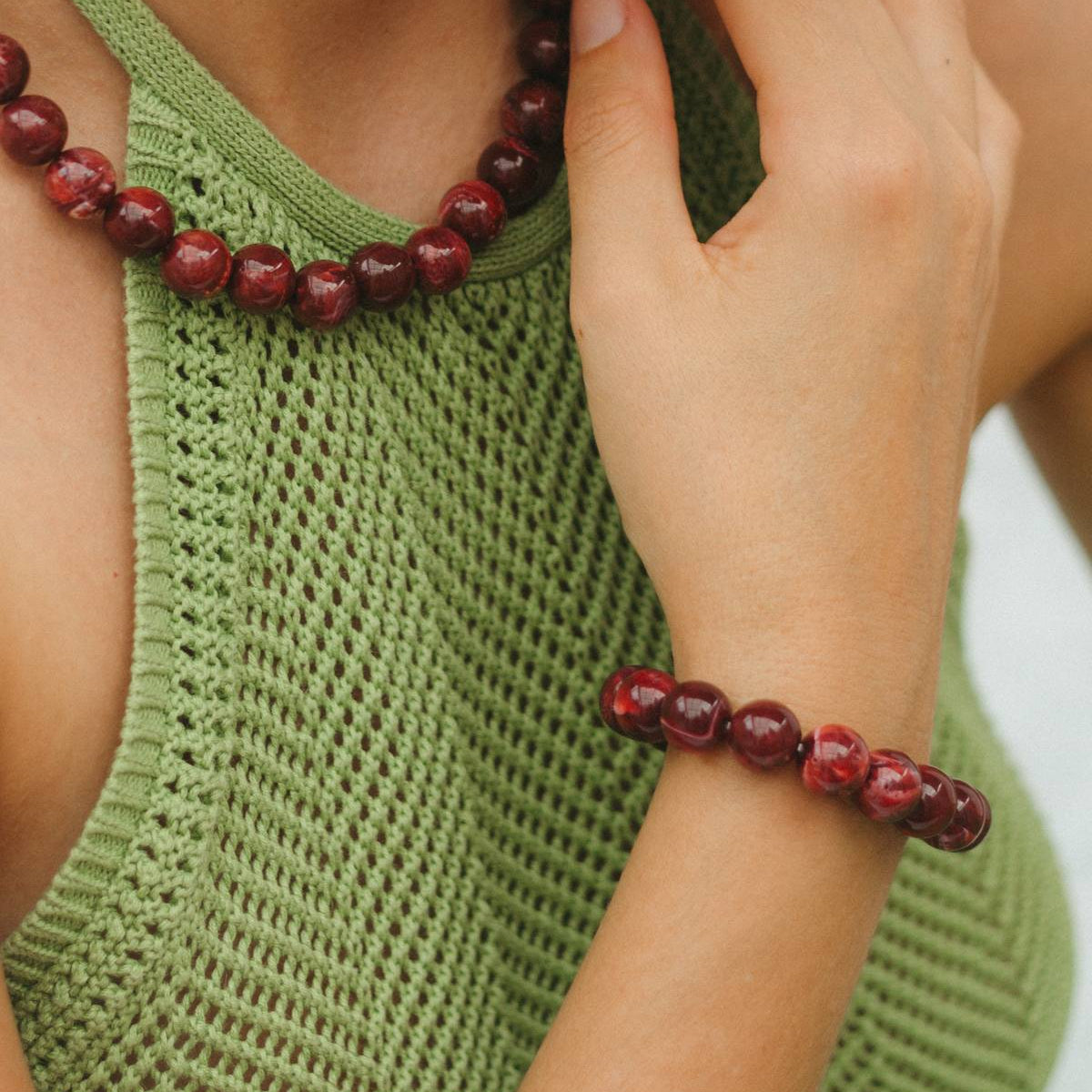 Person wearing a green sleeveless top and red beaded bracelet on a white background