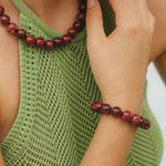 Person wearing a green sleeveless top and red beaded bracelet on a white background