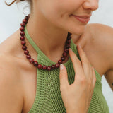 Woman wearing a green sleeveless top and red beaded necklace and bracelet against a neutral background